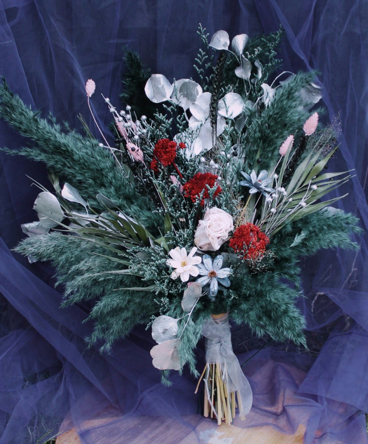 A deep green, white and red dried flower wedding bouquet by Petal Ritual