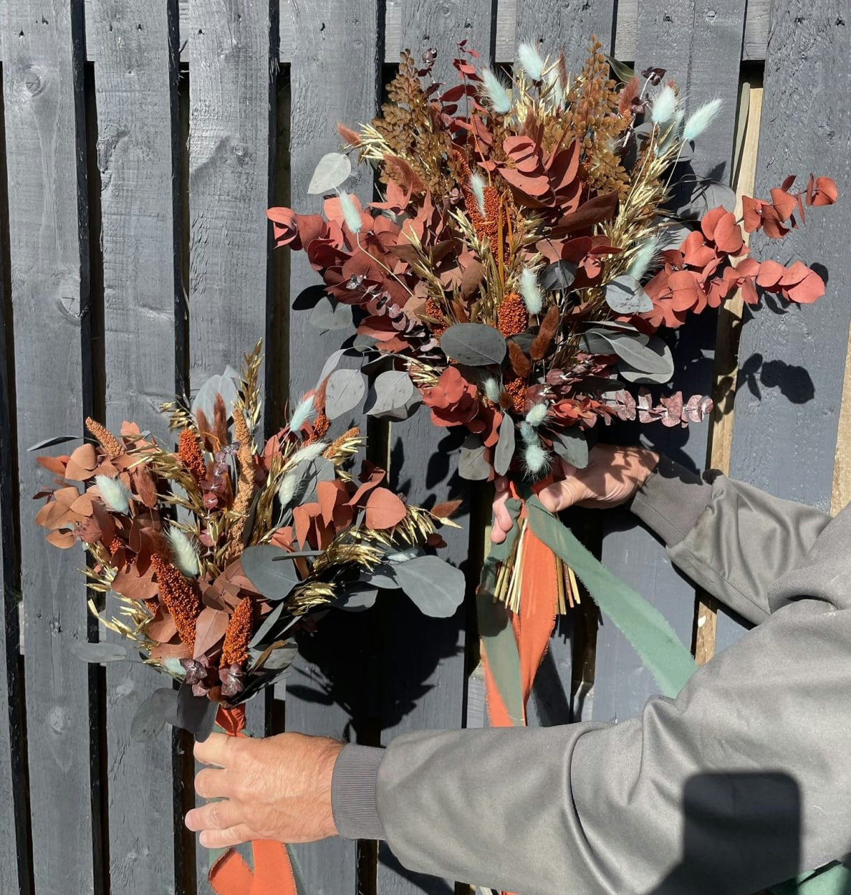 Two rust-toned dried wedding bouquets held against a grey wooden backdrop