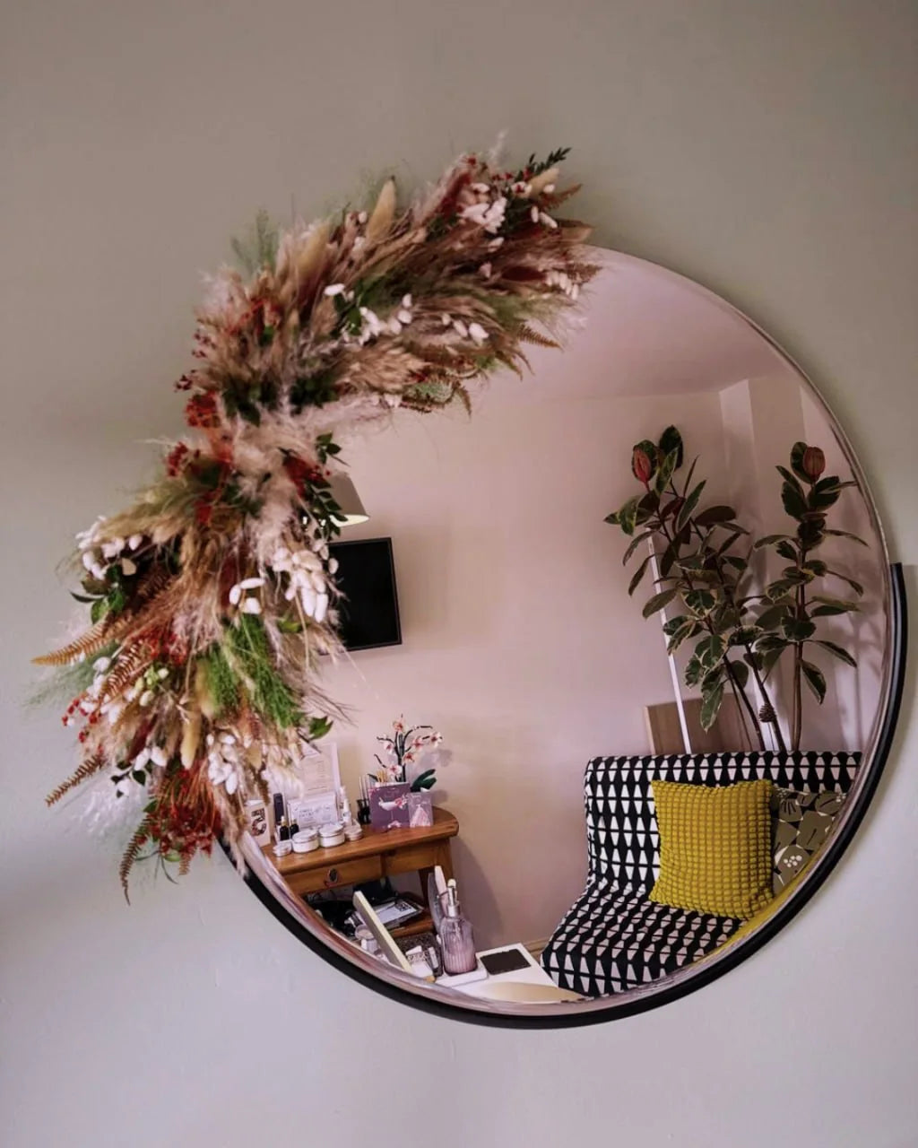 Natural dried-flower installation sweeping around a round mirror